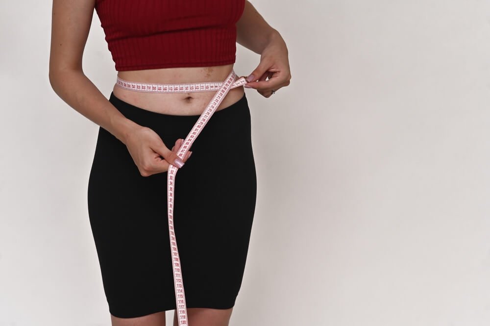 a woman measuring her waist with a tape measure